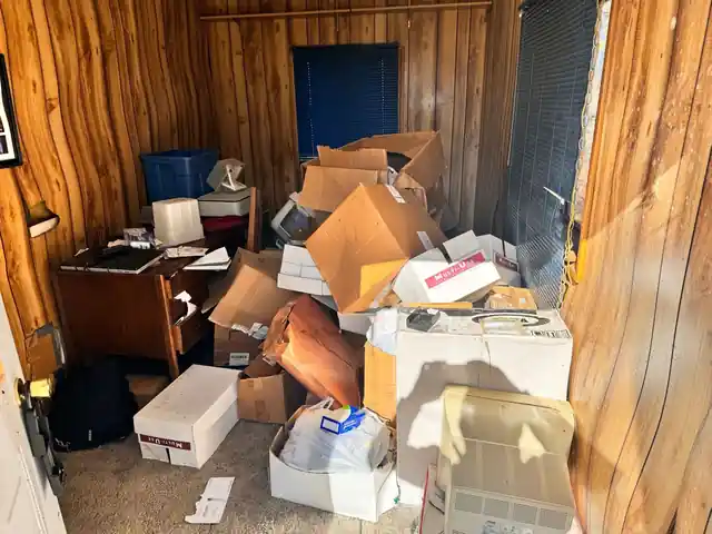 Paneled room with cardboard boxes, a desk and a monitor stacked on grey carpet