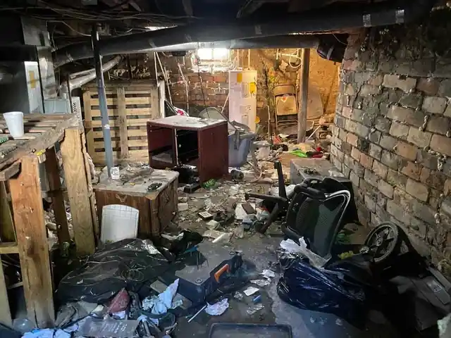Basement with a pallet, a water heater, an office chair and black trash bags against a brick wall