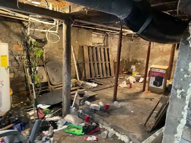 Basement with a pallet against a stone wall, plastic cups and a boxed appliance on the floor