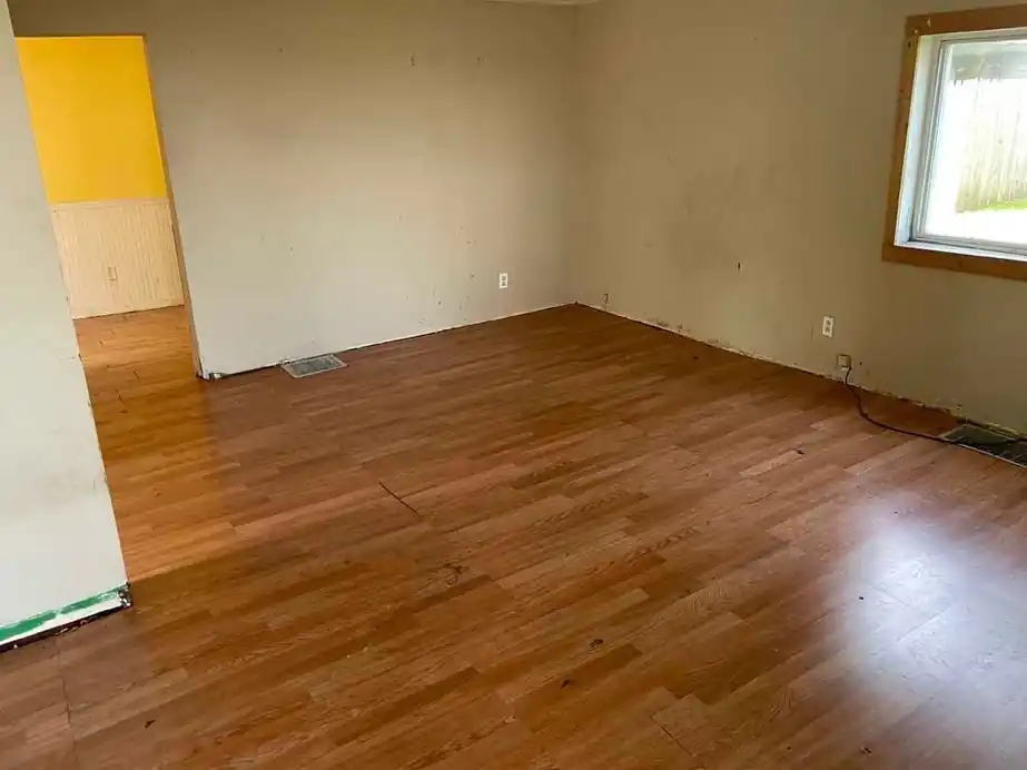 Emptied apartment room with a yellow wall section and swept wood-look floor