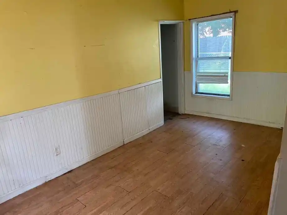 The same yellow room with white wainscot, bare wood floor swept