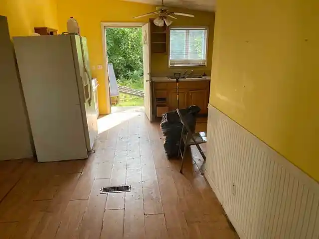 Narrow kitchen with a white refrigerator, yellow wall over white wainscot and a plank floor