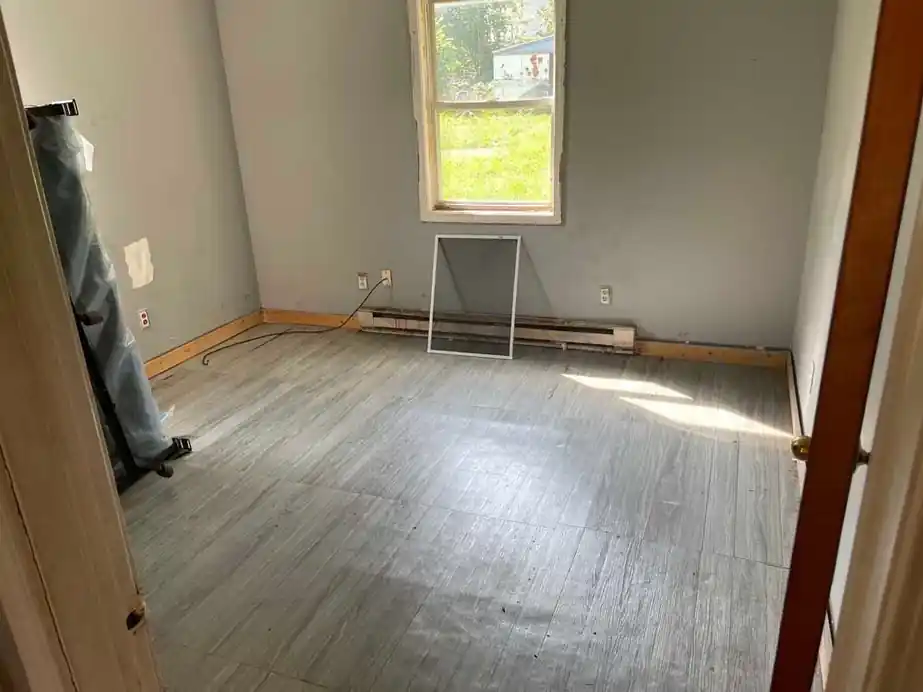Small bedroom with grey plank floor, empty under one window