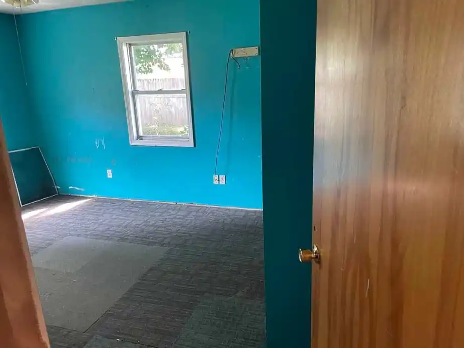 The same teal bedroom emptied to grey carpet tile