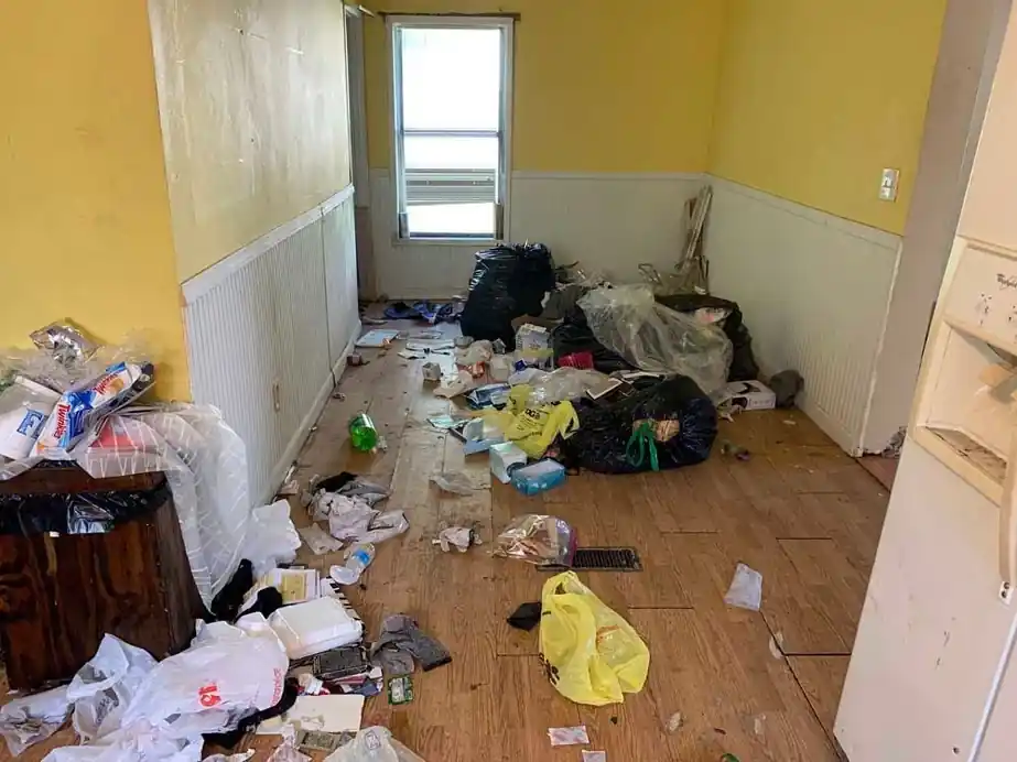 Yellow-walled room with white wainscot, floor covered in bags and trash