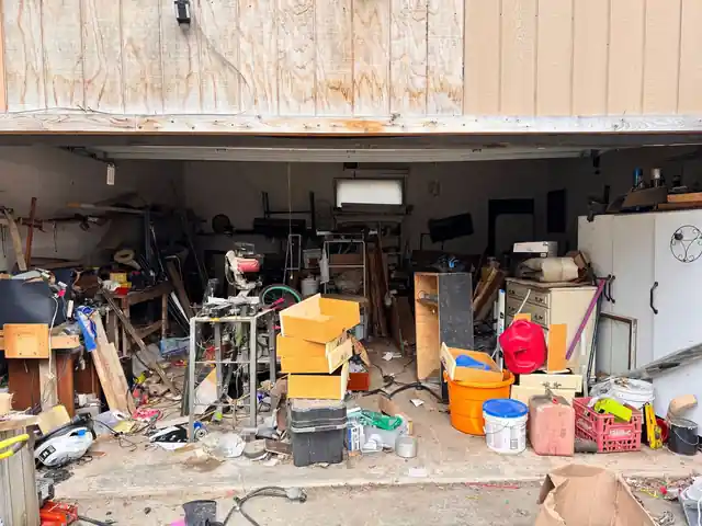 Open two-car garage packed with shelving, a chop saw, buckets, boxes and a white refrigerator