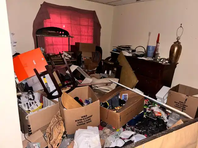 Room with a dresser, cardboard boxes, a broken chair and loose items across the floor