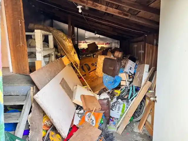 Shed stacked to the rafters with plywood sheets, a bicycle wheel, a brown case and bagged material