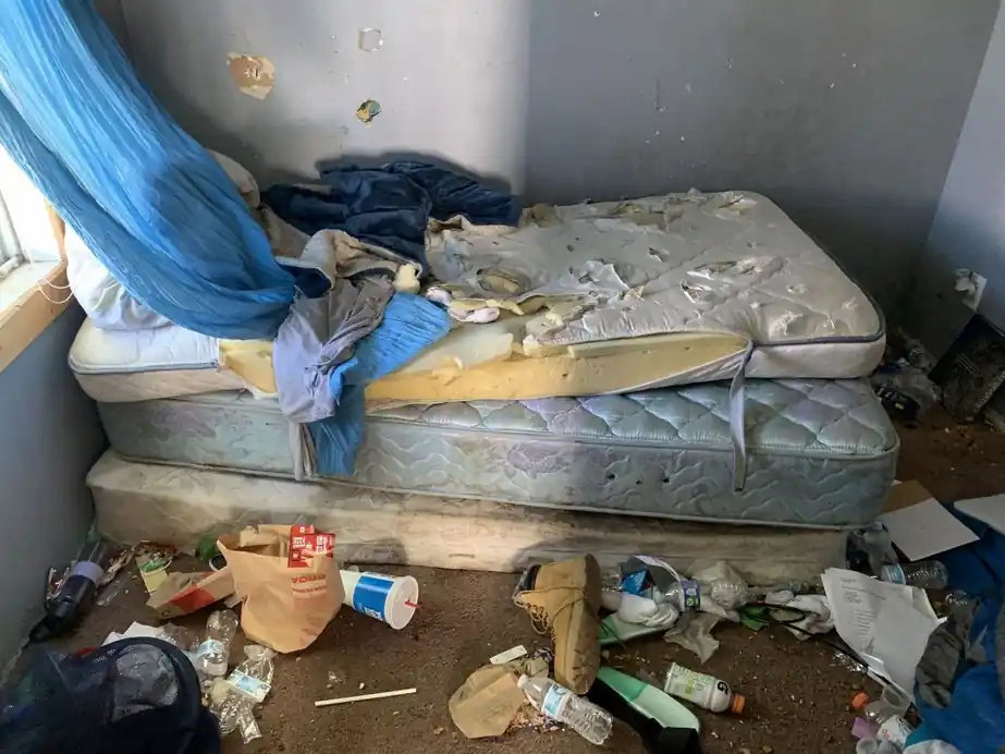 Torn mattress and scattered trash left in a bedroom by a former tenant