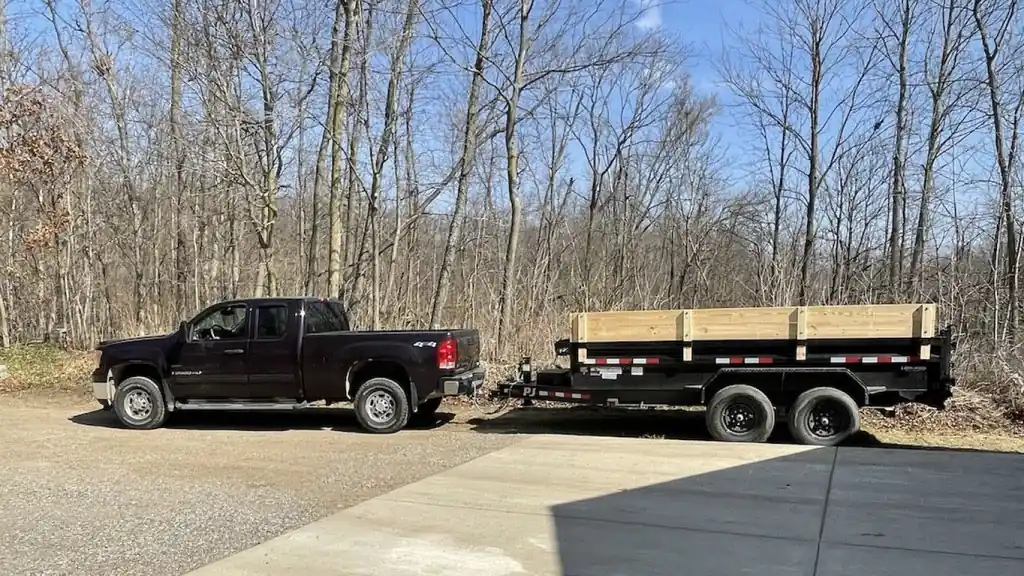 Black pickup truck hitched to an empty black dump trailer on a gravel lot
